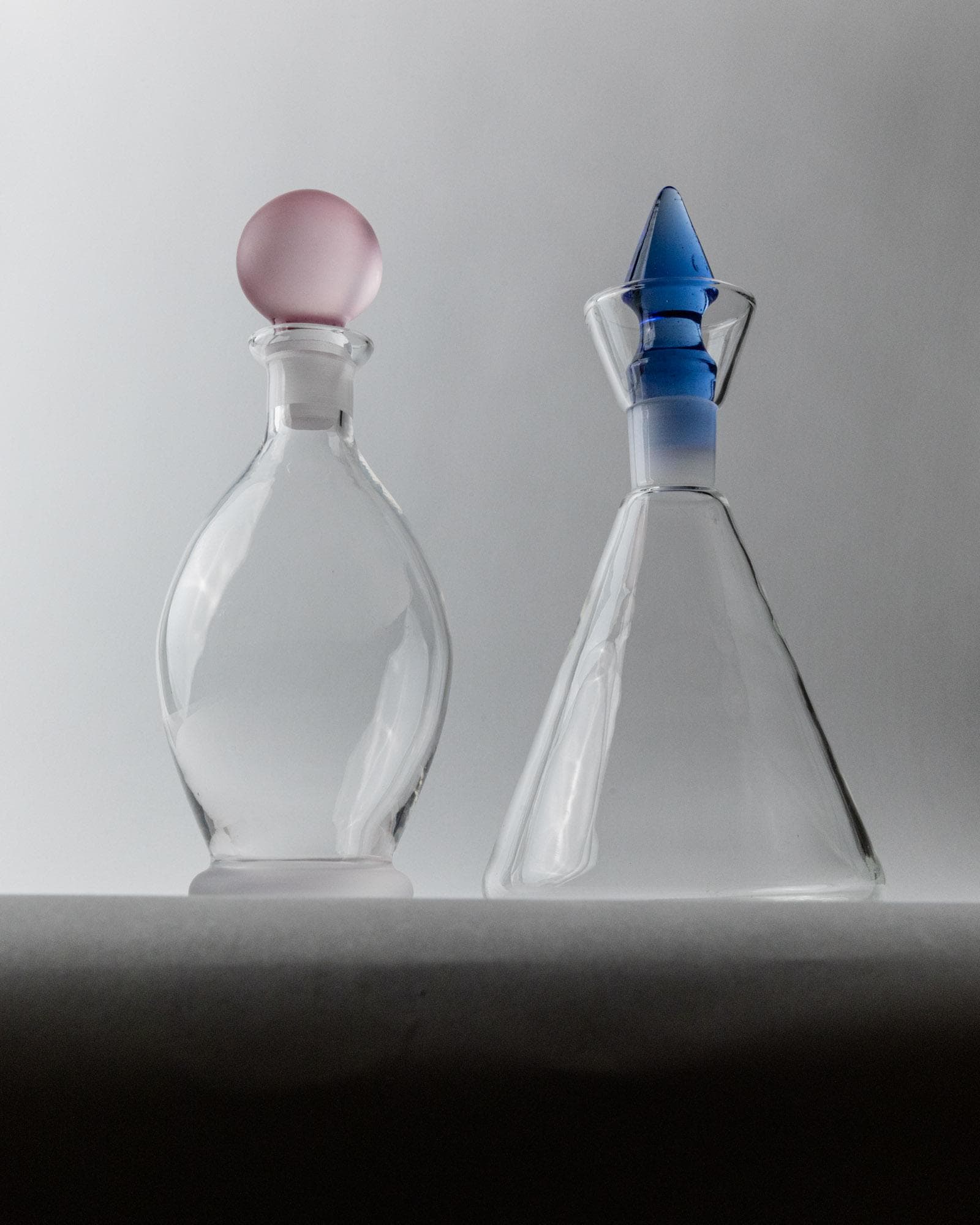 Vintage 1980s Glass Decanter Set of 2, Clear Glass with pink, blue Stoppers, Different Sculptural Shapes, Bar Accessory, Elegant Gift Idea_Bottega Jacobs